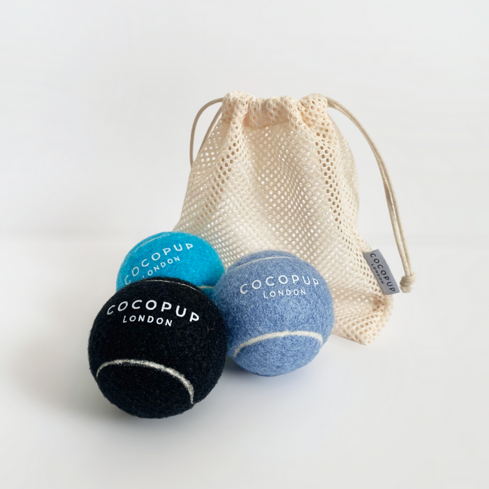 Set of three Cocopup London tennis balls in black, light blue, and bright blue with a beige mesh carry bag.