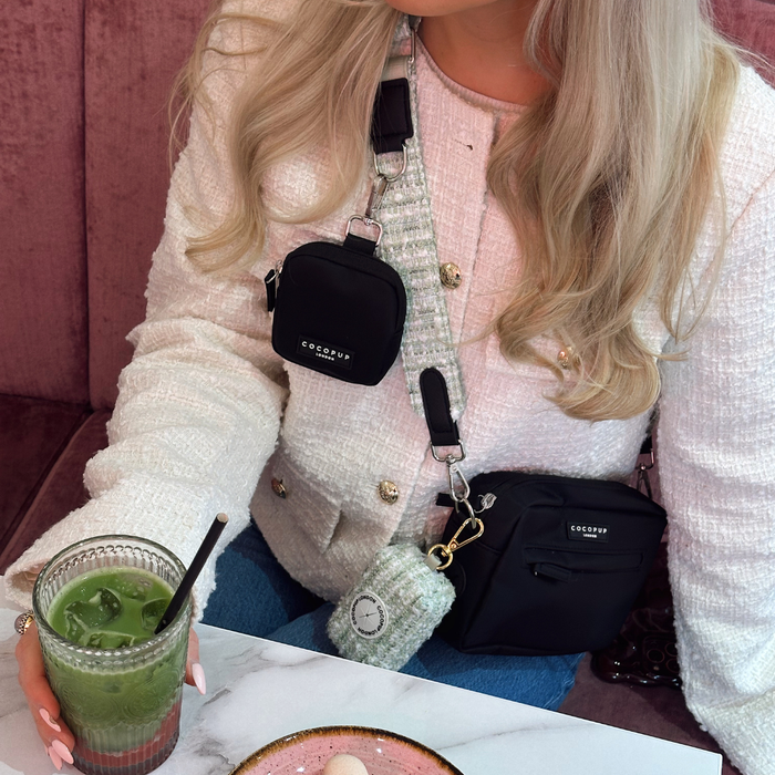 Woman with long blonde hair sips matcha, wearing blue jeans and a green textured tweed bag strap.