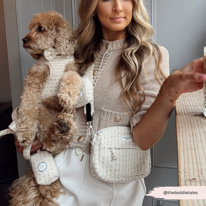 Woman in vanilla textured tweed holds a dog in a matching vest, carrying a beige Cocopup London dog walking bag.
