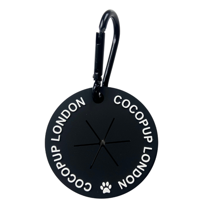 Black, round Cocopup London dog walking bag with carabiner clip, white paw print, and central slit opening.