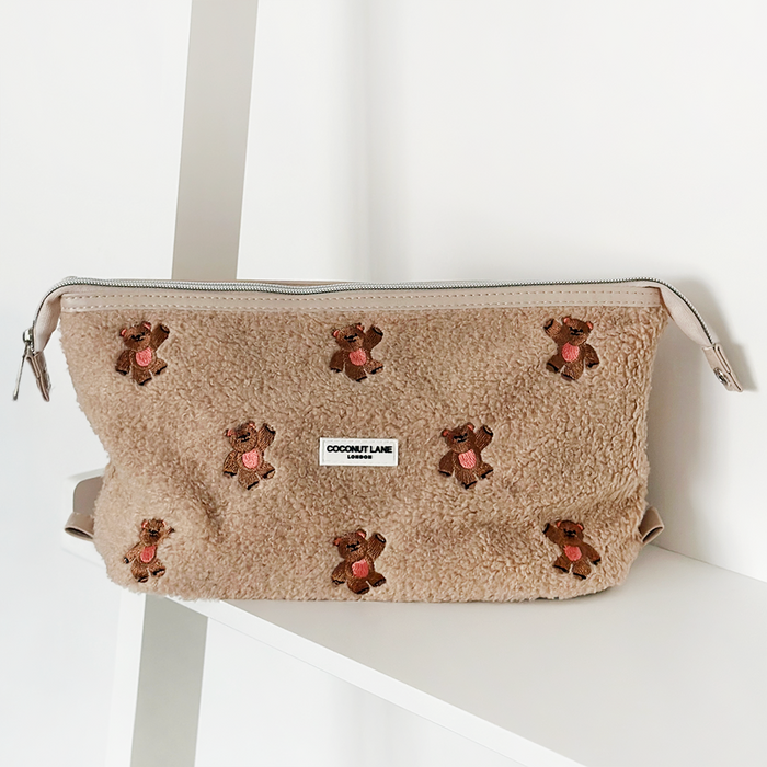 Beige embroidered teddy-texture expandable makeup bag with Theo design, displayed on a white shelf.