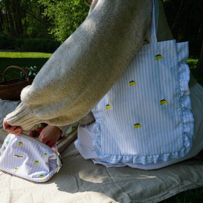 Person on picnic blanket with yellow lemon-print Cocopup tote bag and matching pouch.