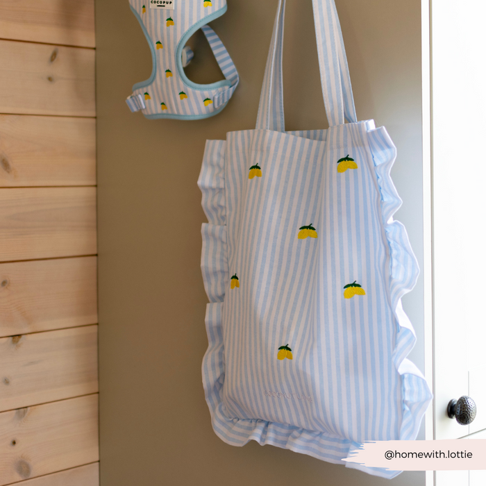 Blue and white striped Cocopup London tote bag with ruffles and lemon print, hanging by a matching harness.