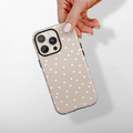 Hand holding beige Cocopup London Tough Phone Case with small white hearts pattern against a plain background.