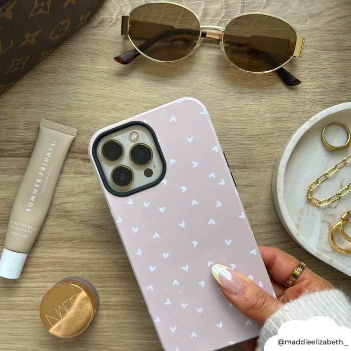 Hand holding a Cocopup London Tough Phone Case with chai-colored heart pattern, surrounded by accessories.