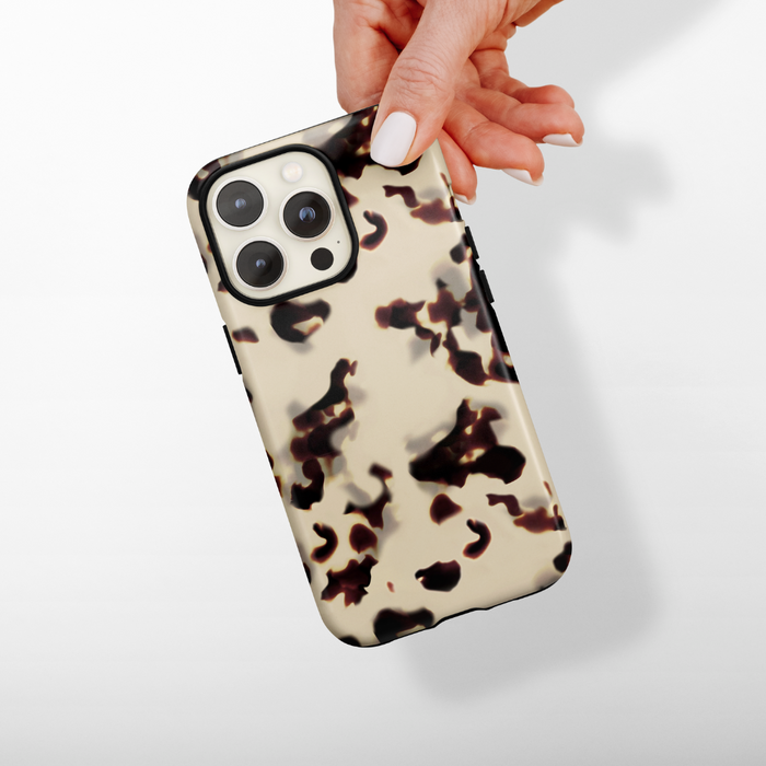 Hand holding Cocopup Londons beige and brown tortoiseshell phone case against a white background.