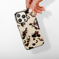 Hand holding Cocopup Londons beige and brown tortoiseshell phone case against a white background.