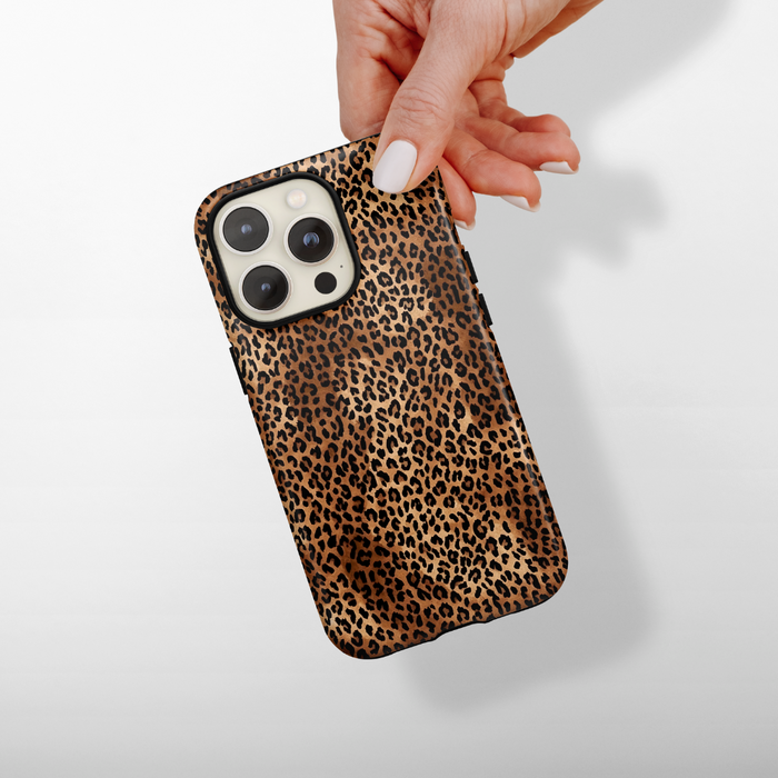 Hand holding a smartphone in a Cocopup London Leopard Pup tough case against a light background.