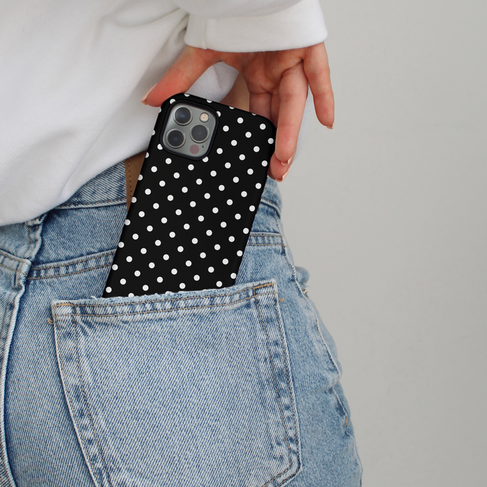 Hand holding a Cocopup London tough phone case with black polka dots, placing it into blue jeans back pocket.