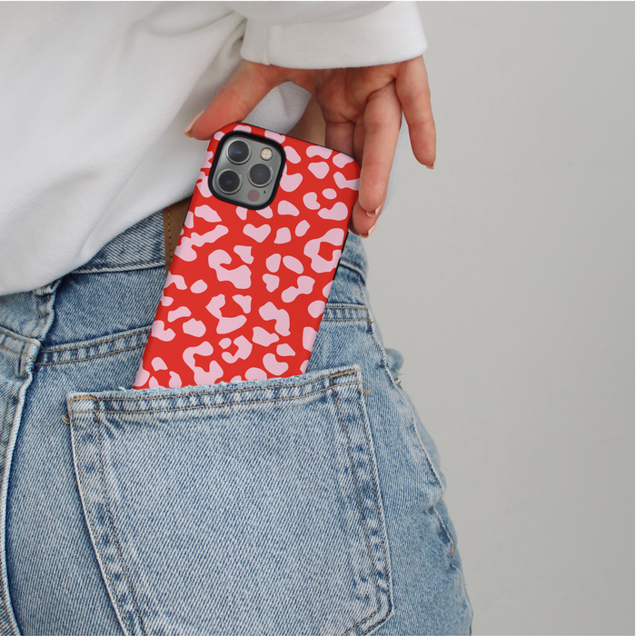 Red and pink leopard print phone case with heart accents partially visible in a blue denim jean pocket.