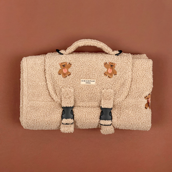 Beige fuzzy bag with teddy bear patches and black buckles.