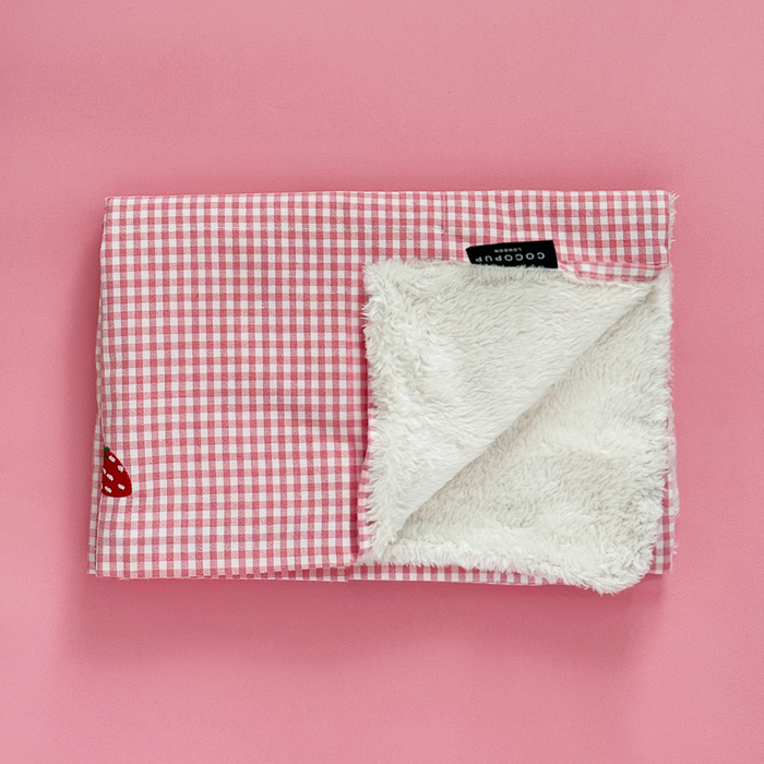 Folded Cocopup London Strawberry Picnic travel mat and blanket set with fluffy lining on a pink background.