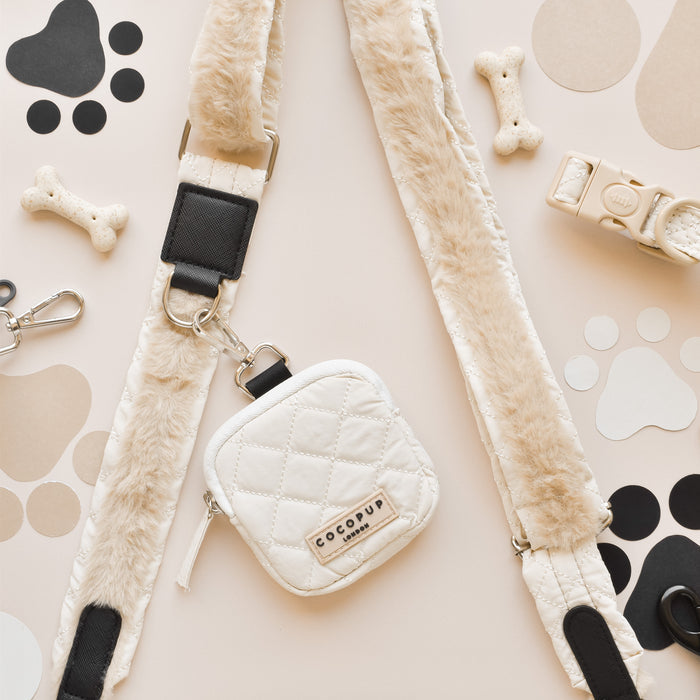Cream quilted Cocopup London treat pouch with faux fur, shown with bone treats and paw prints on a beige background.