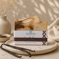 Bar of soap with 'OldSoul' packaging on a stone surface with vanilla beans and a vase in the background.