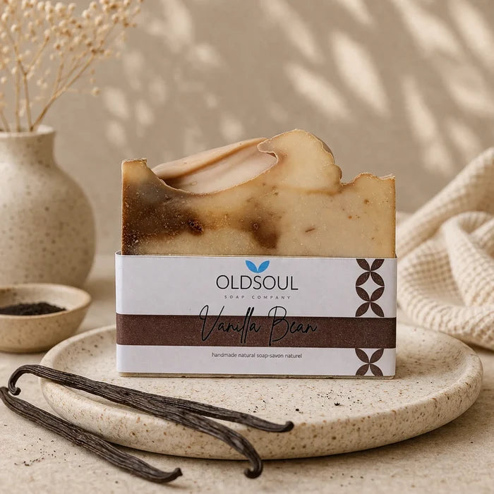 Bar of soap with 'OldSoul' packaging on a stone surface with vanilla beans and a vase in the background.