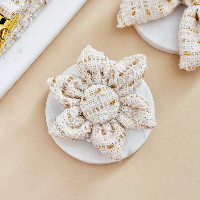 Cream and gold textured tweed collar flower resting on a white marble plate.