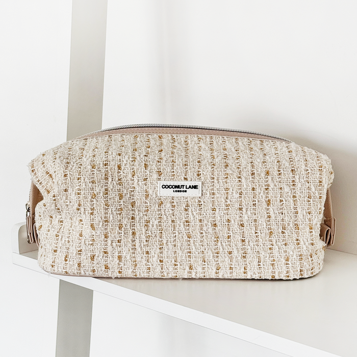 Vanilla textured tweed expandable makeup bag with a zipper, displayed on a white shelf.
