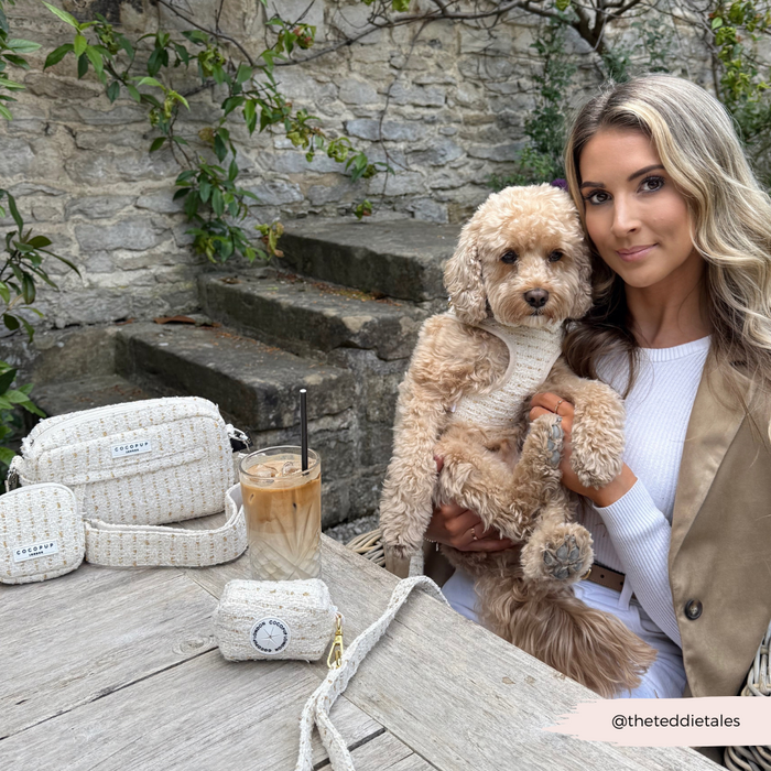 Woman carrying a vanilla tweed Cocopup London dog walking bag, holding iced coffee, with a curly-haired dog.