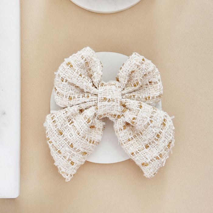 Cream and gold textured tweed sailor bow tie on a round white surface.