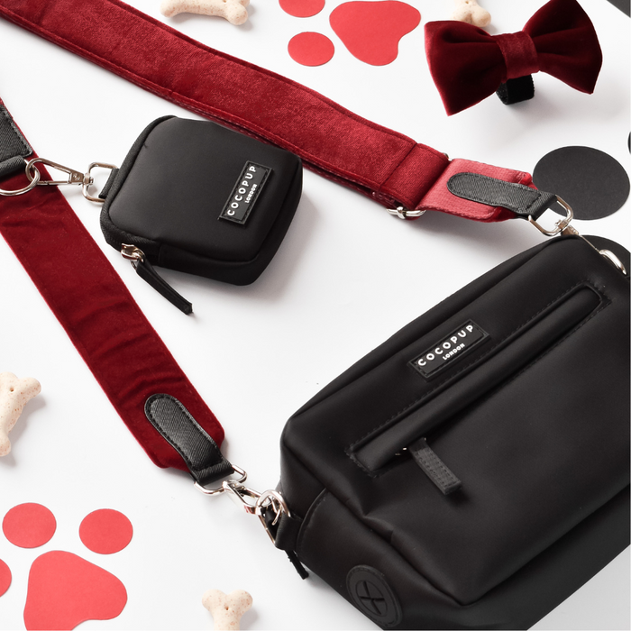 Berry red Cocopup London walking bag with velvet strap, shown with a red bow tie, dog bone treats, and paw prints.