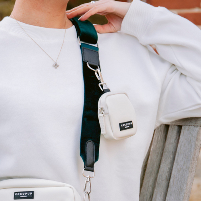 Person in a white sweater sitting on a bench with a Cocopup London Dog Walking Bag and green velvet bag strap.