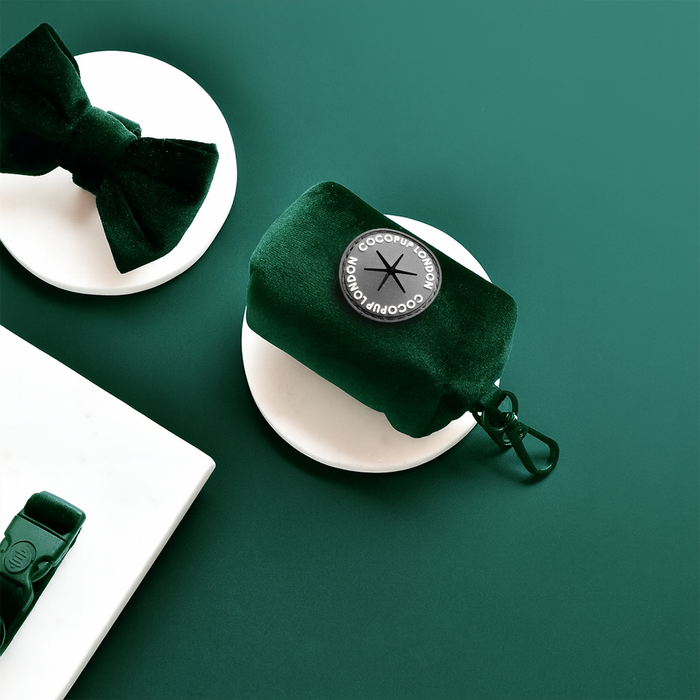 Forest green velvet poop bag holder displayed on marble pedestals with a matching green background.
