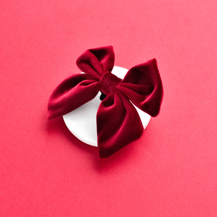 Berry red velvet sailor bow tie on a round white platform with a pink background.