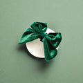 Forest green velvet sailor bow tie rests on a round white surface with a solid green background.