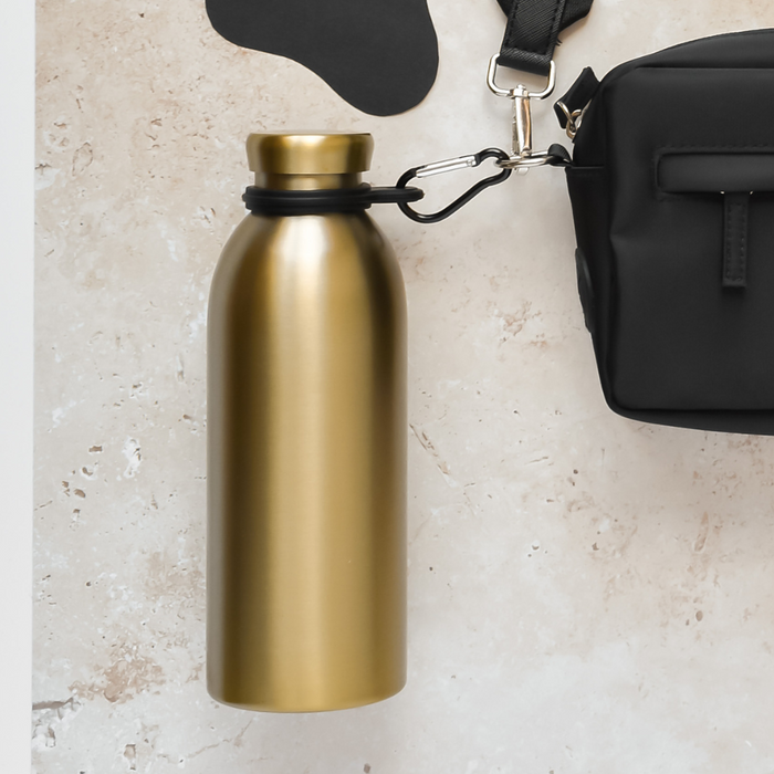 Gold water bottle clipped to a black bag with a Cocopup London holder, set against a light textured background.