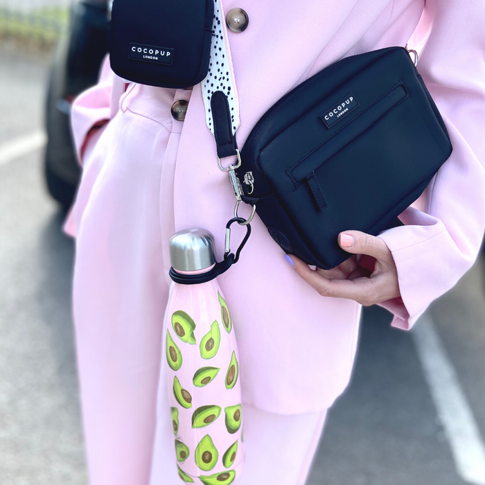 Person in a pink suit carries a black bag with a Cocopup London water bottle holder clip attached.