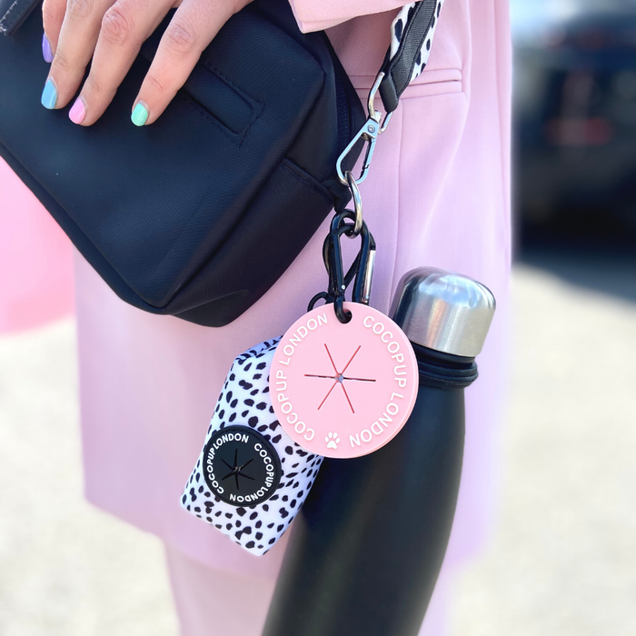 Black bag with pink Cocopup London tag and Water Bottle Holder Clip, held by a person wearing pink.